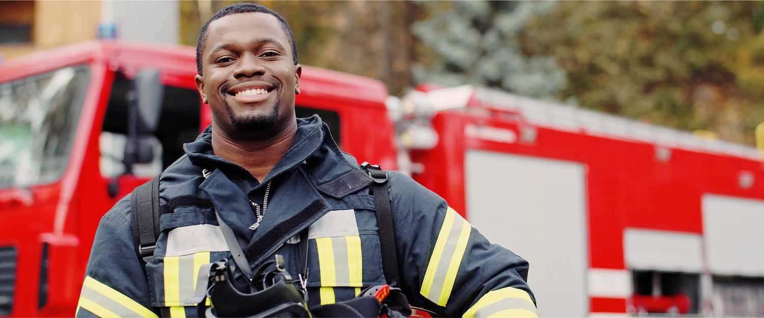 Firefighter portrait on duty. Photo of happy fireman with gas mask and helmet near fire engine